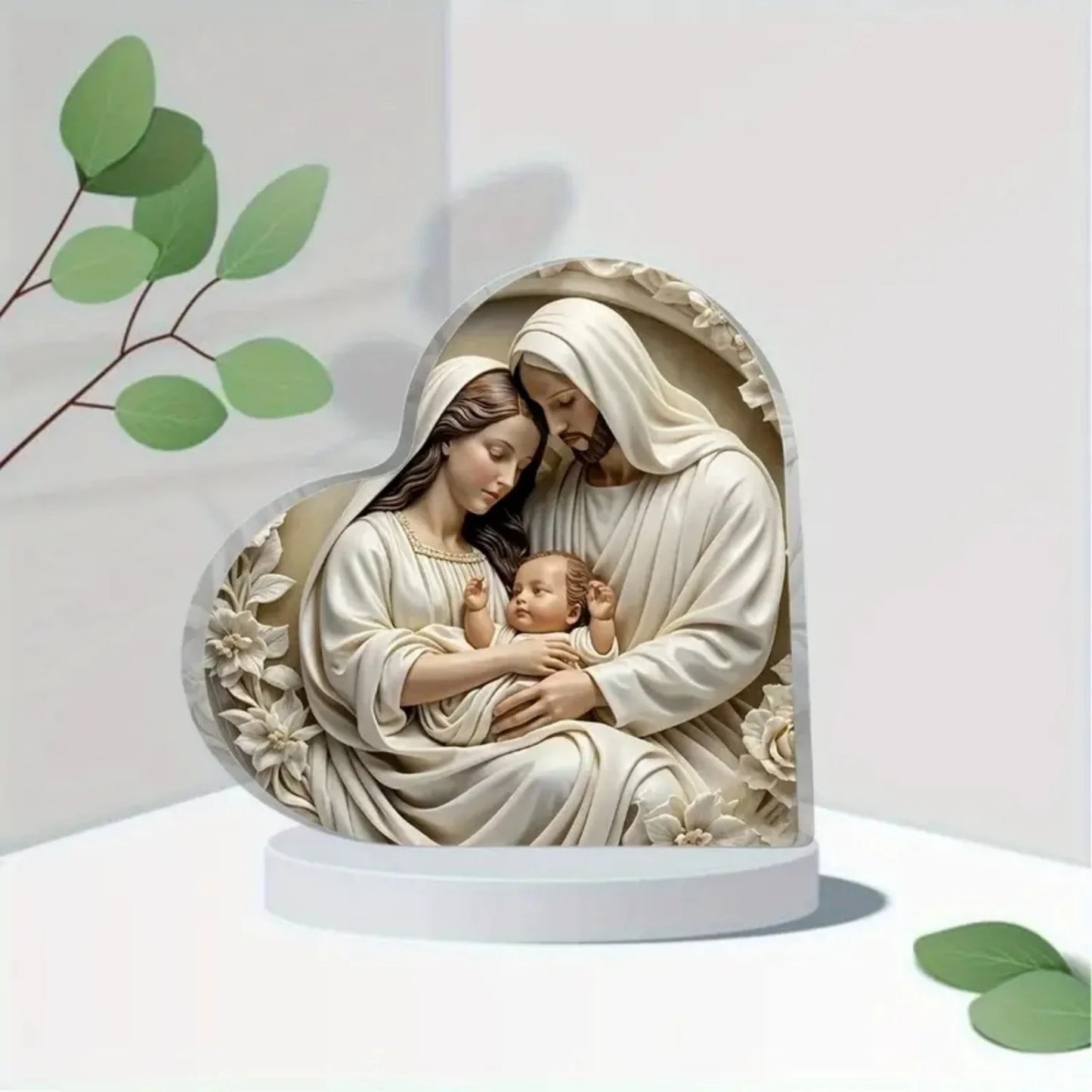 Statue of a religious scene with two figures holding a baby, surrounded by green leaves on a white background.